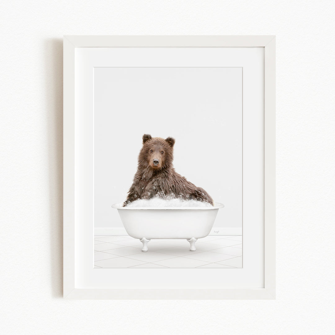 A brown bear sitting in a white bathtub filled with bubbles, looking directly at the camera.