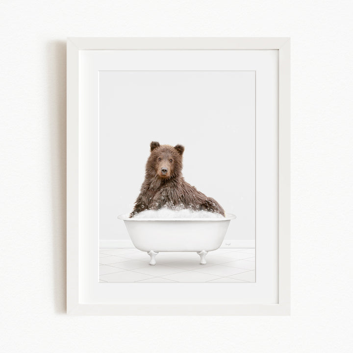 A brown bear sitting in a white bathtub filled with bubbles, looking directly at the camera.