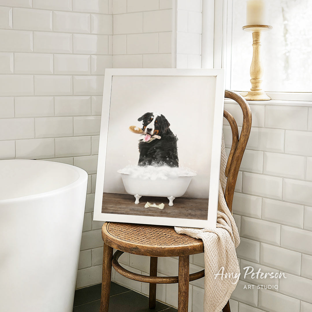 A framed photograph of a dog sitting in a bathtub, with a towel draped over the back of a wooden chair in a bathroom setting.