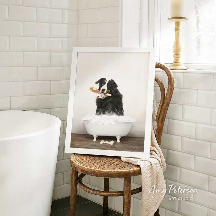 A framed photograph of a dog sitting in a bathtub, with a towel draped over the back of a wooden chair in a bathroom setting.