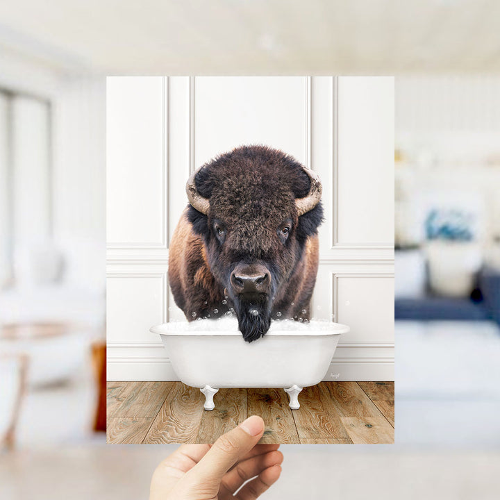 A large, furry bison with horns is sitting in a white bathtub, surrounded by a blurred background.