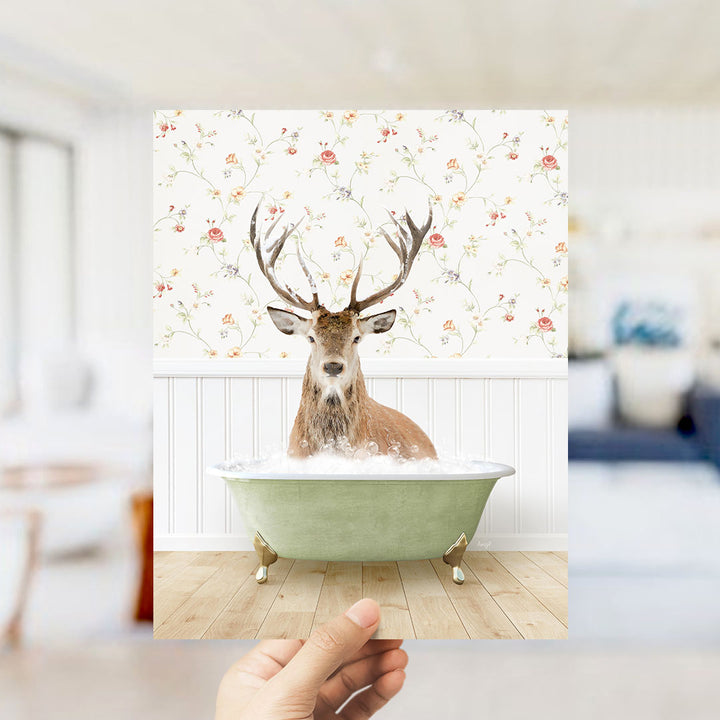 A deer with antlers is sitting in a green bathtub filled with bubbles, against a floral wallpaper backdrop.