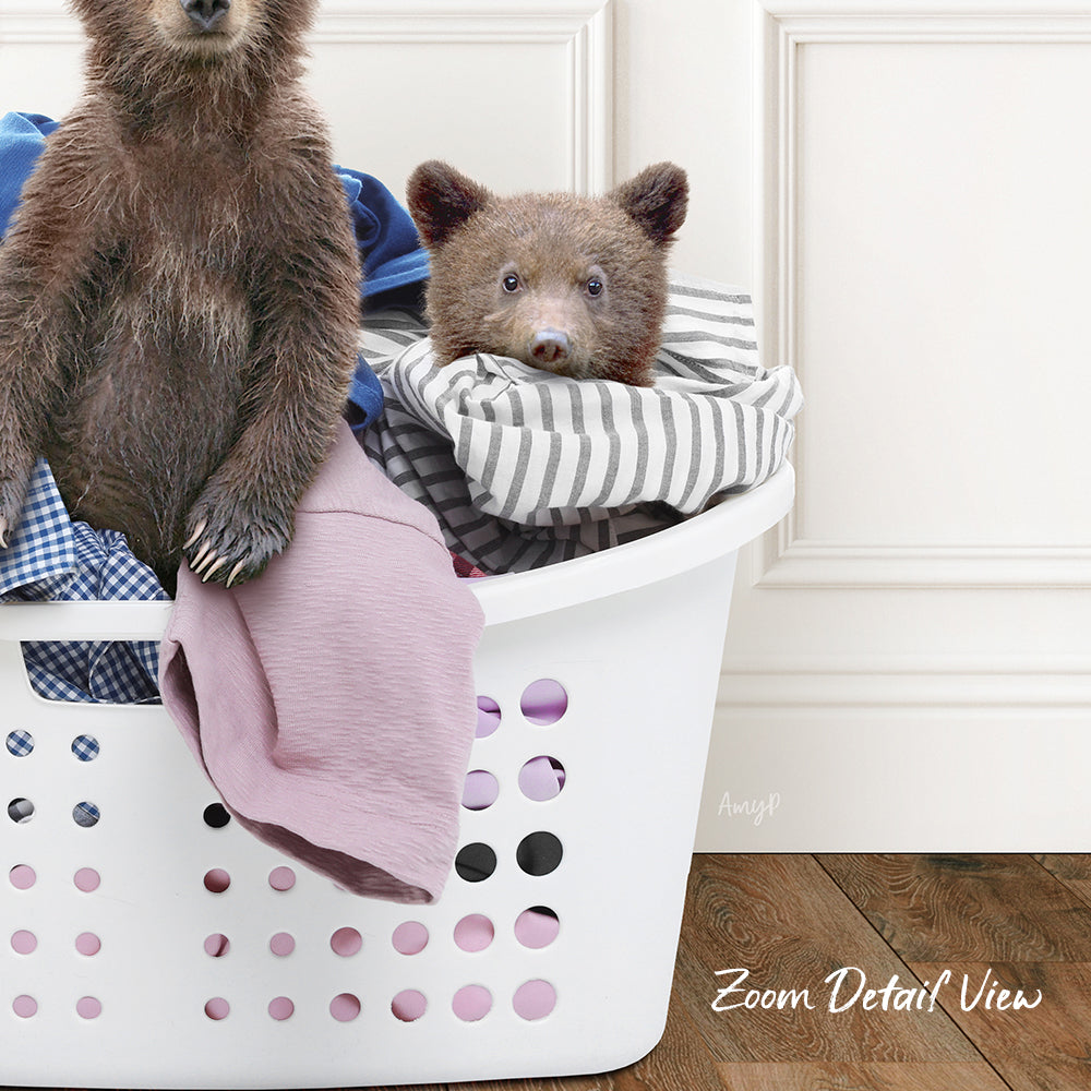A brown bear sitting in a laundry basket filled with clothes, with a smaller bear's head peeking out from the clothes.