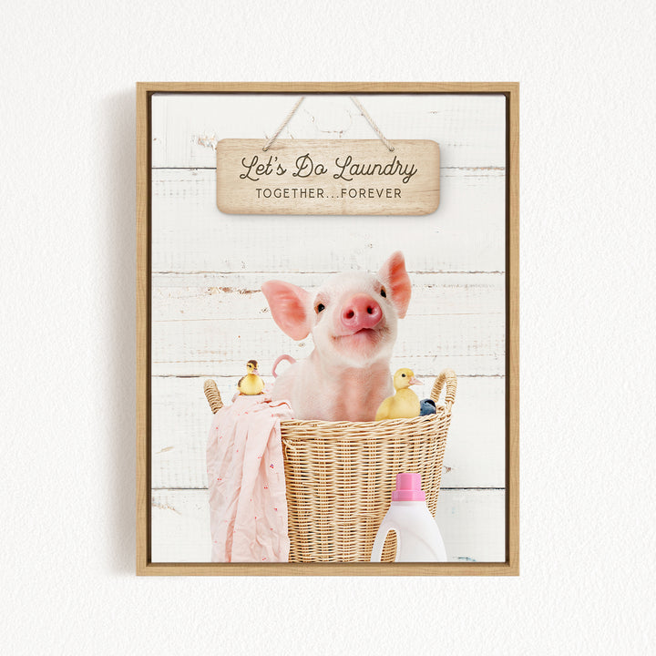 A cute pig sitting in a wicker basket filled with various toys, including a yellow duck and a pink blanket, with a wooden sign above that says "Let's Da Laundry Together Forever".