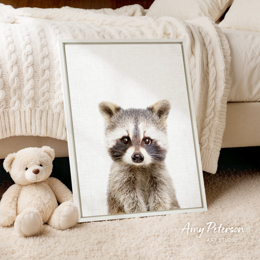 A framed photograph of a raccoon is displayed on a bed, accompanied by a teddy bear.