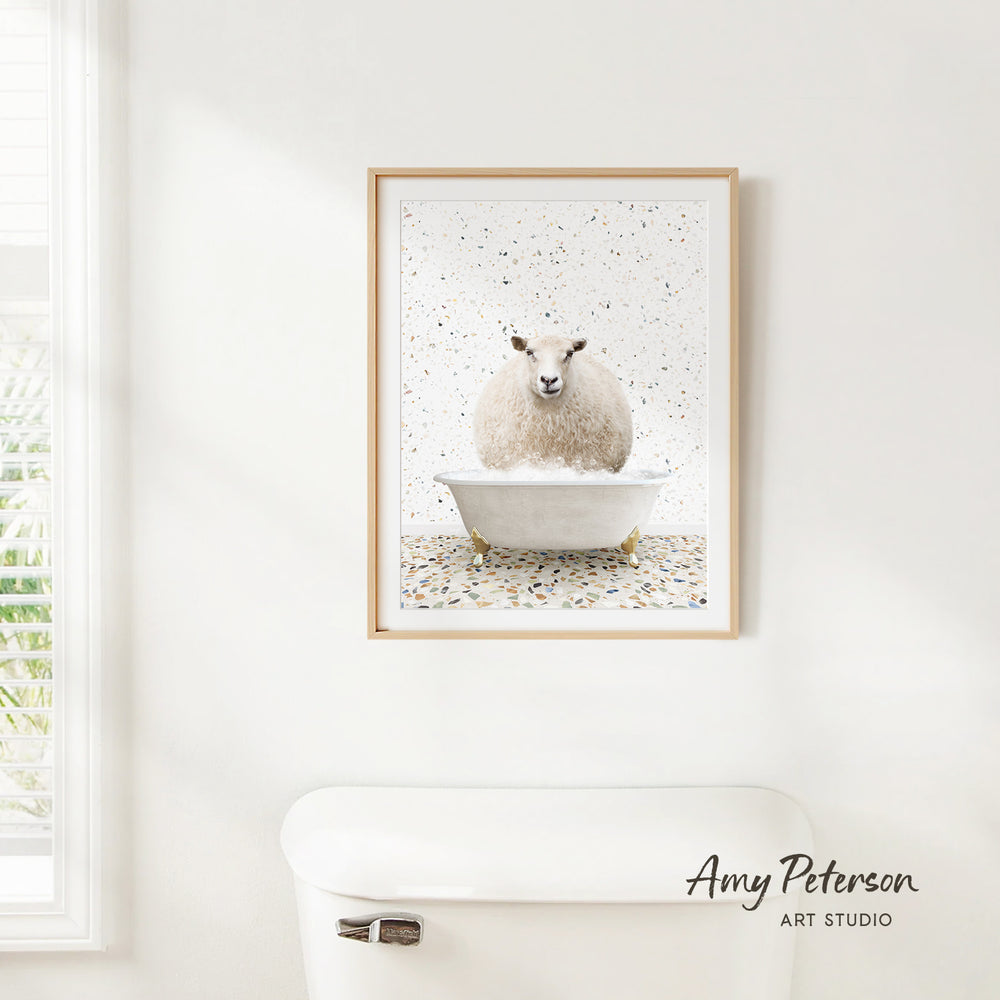 A framed print of a sheep sitting in a bathtub is hanging on a white wall in a bathroom.