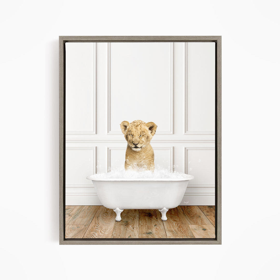 A young lion cub sitting in a white bathtub filled with water, looking at the camera with a playful expression.