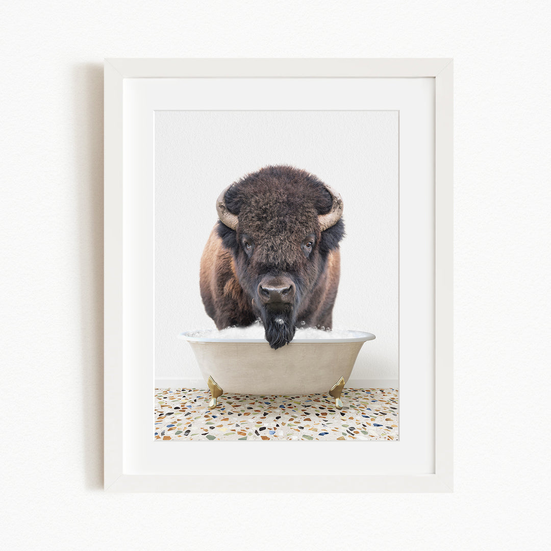 A bison with large horns is standing in a white bathtub filled with water, appearing to be enjoying a bath.
