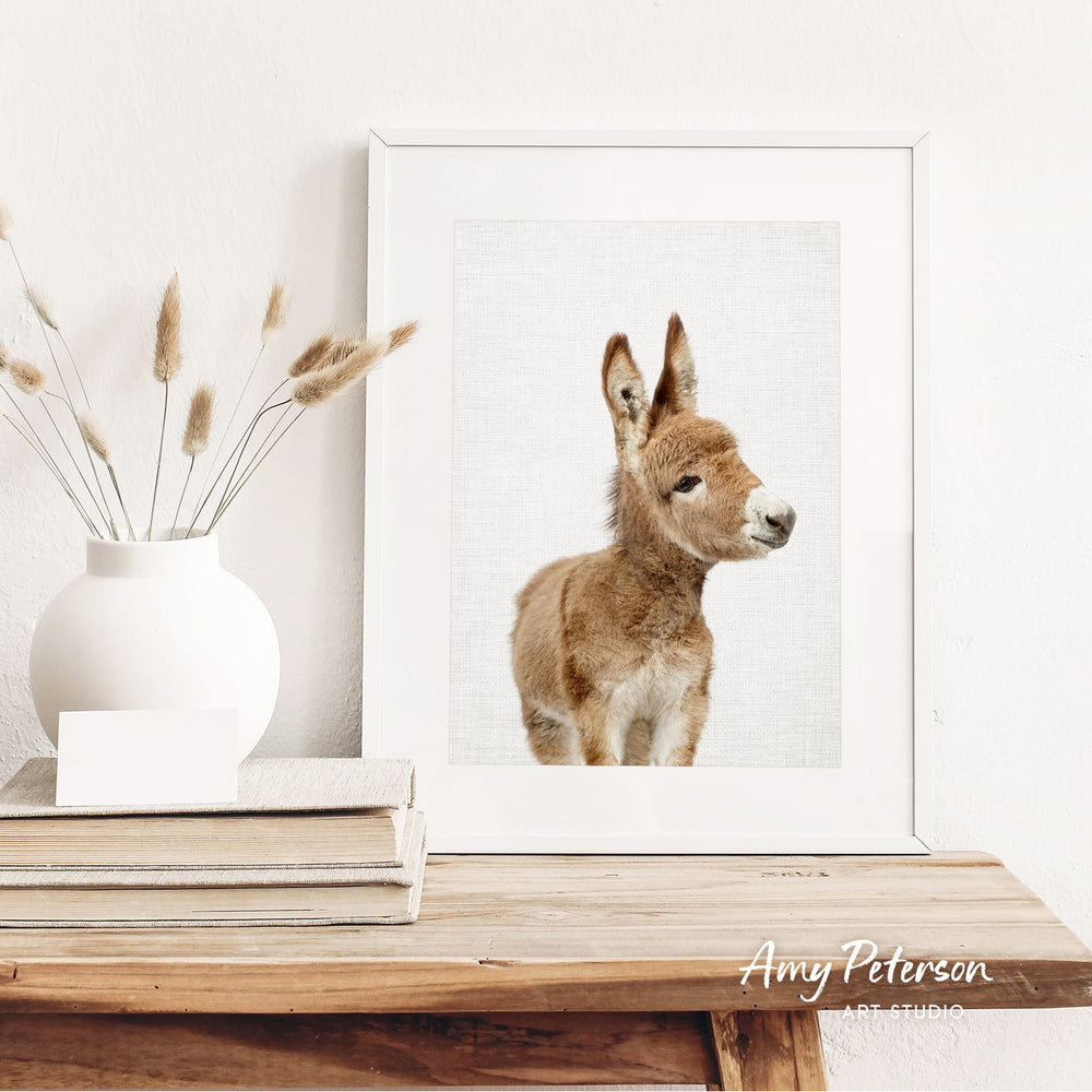a white vase with dried reeds, a framed picture of a brown animal, and a stack of books on a wooden shelf.