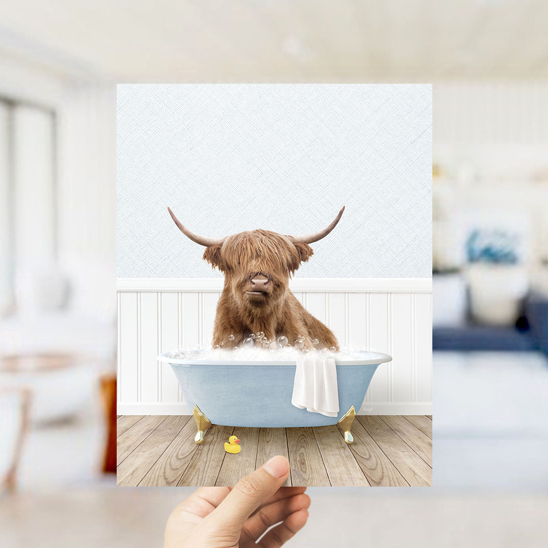 A brown cow with long horns is sitting in a blue bathtub filled with bubbles, with a yellow rubber duck floating nearby.