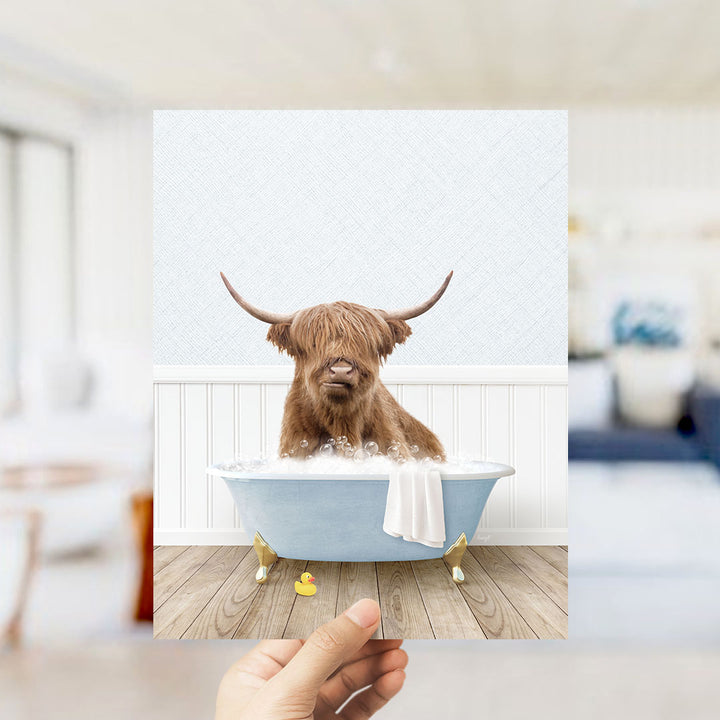 A brown cow with long horns is sitting in a blue bathtub filled with bubbles, with a yellow rubber duck floating nearby.