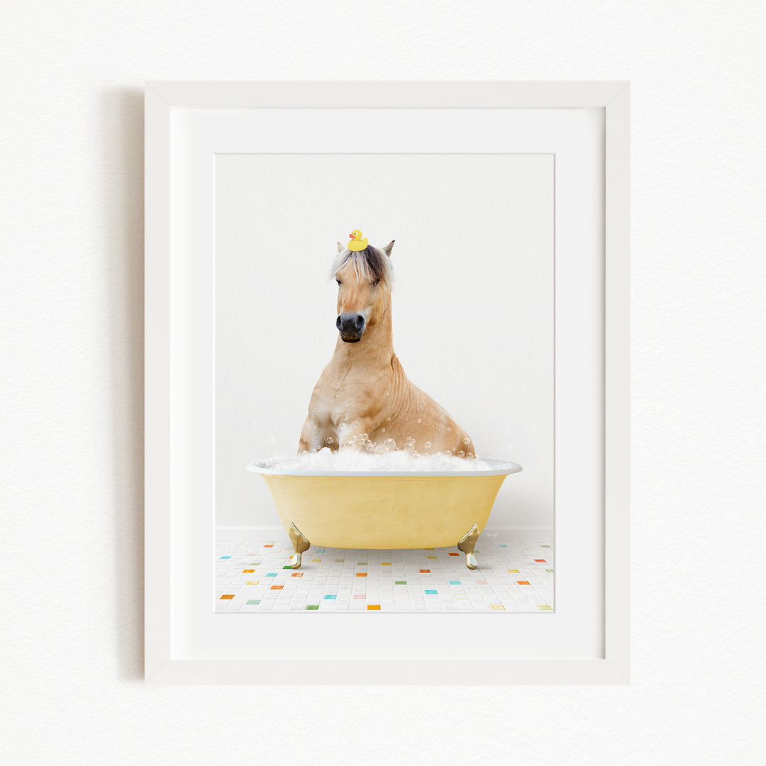 A light brown horse is sitting in a yellow bathtub filled with bubbles, with a yellow rubber duck perched on its head.
