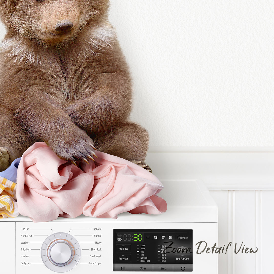 A brown bear sitting on a pile of clothes next to a washing machine.
