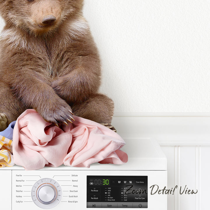 A brown bear sitting on a pile of clothes next to a washing machine.