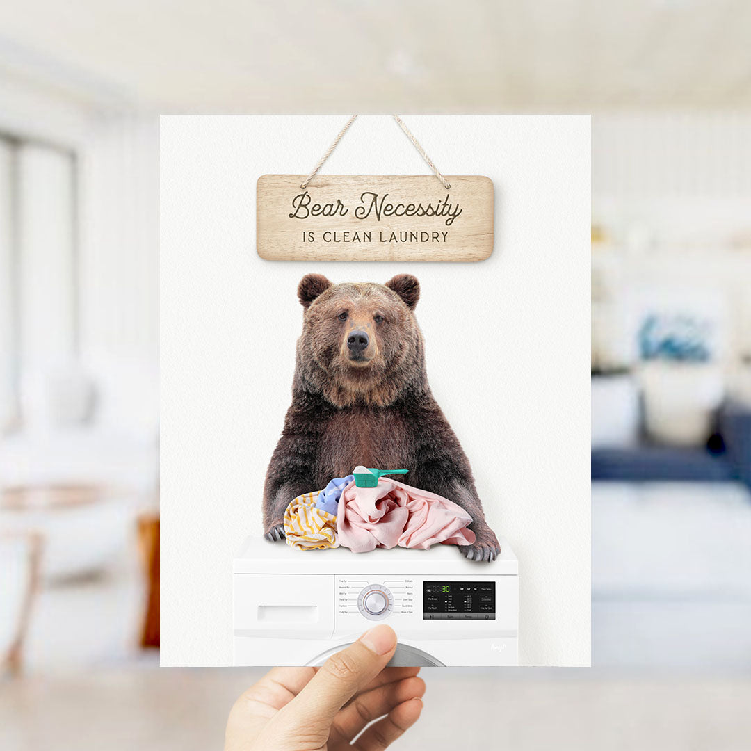 A wooden sign with the text "Bear Necessity is Clean Laundry" hangs above a washing machine with a bear sitting on top of it.