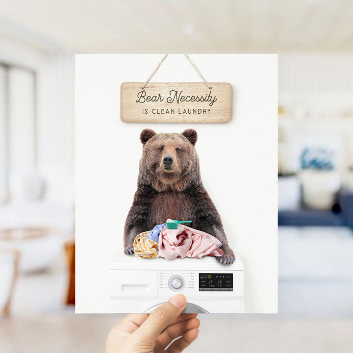 A wooden sign with the text "Bear Necessity is Clean Laundry" hangs above a washing machine with a bear sitting on top of it.
