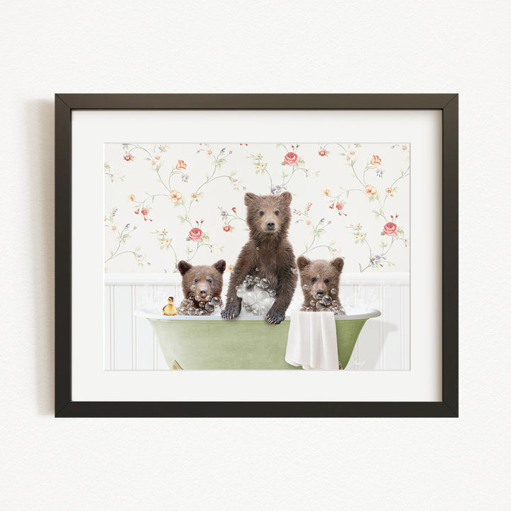 A framed image depicting three bears sitting in a green bathtub, with a floral pattern on the wall behind them.
