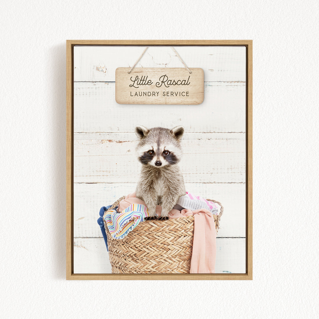 A raccoon sitting in a woven laundry basket, with a sign above that reads "Little Racal Laundry Service".