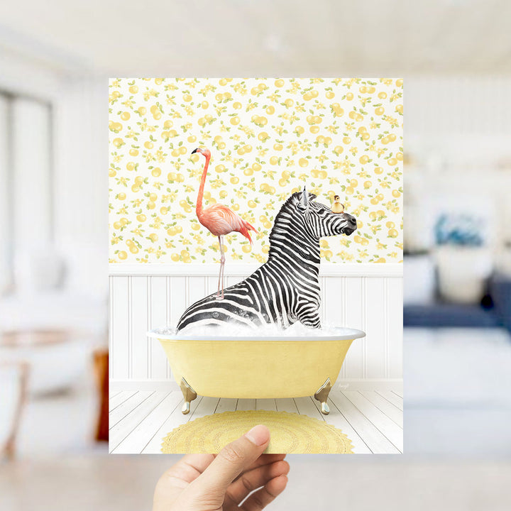 A hand holds up a print featuring a zebra sitting in a yellow bathtub, with a pink flamingo standing on its back.