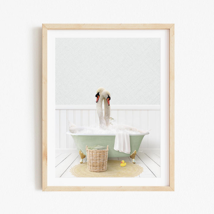 A framed image depicting a pair of swans sitting in a green bathtub filled with bubbles, surrounded by a basket of rubber ducks and a towel.