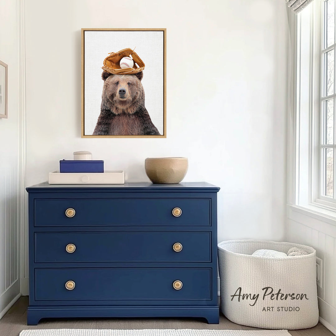 a framed picture of a bear wearing a baseball cap, placed on a blue dresser in a room with white walls and a window.