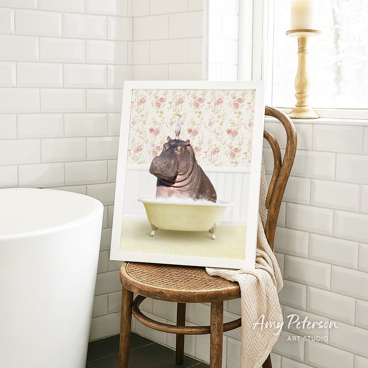 A framed image of a hippopotamus sitting in a bathtub is displayed on a wooden chair in a bathroom setting.