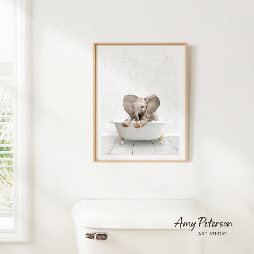 A framed image of an elephant sitting in a bathtub, with its trunk raised, is hanging on a white wall.