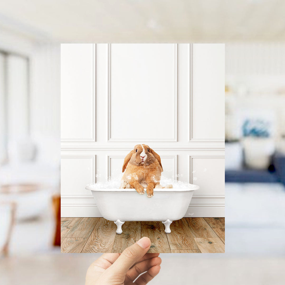A brown rabbit sitting in a white bathtub filled with water, with bubbles around it, in a room with white walls and a wooden floor.