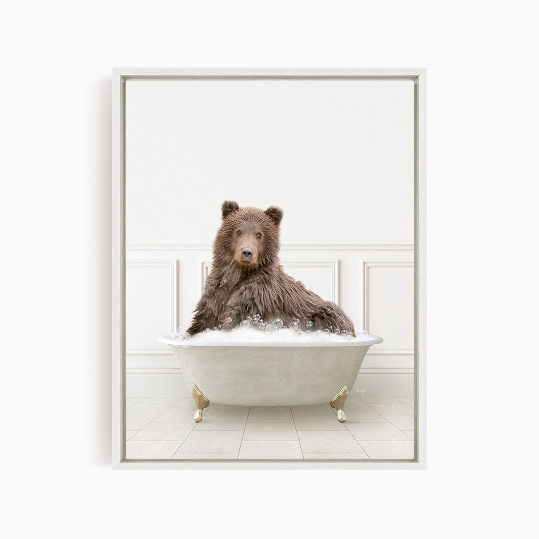 A brown bear sitting in a white bathtub filled with bubbles, looking directly at the camera.
