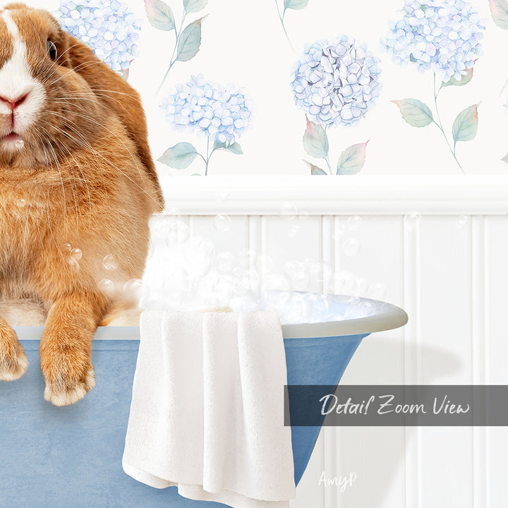 A brown rabbit sitting in a blue bathtub filled with bubbles, with a towel and a floral patterned wall in the background.