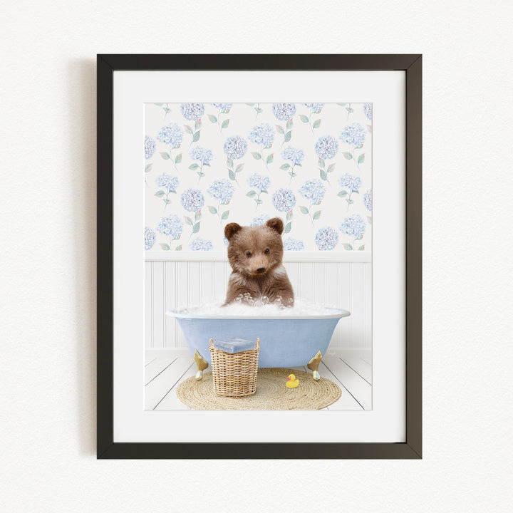 A brown bear sitting in a blue bathtub filled with bubbles, surrounded by a floral patterned wall and a basket of rubber ducks.