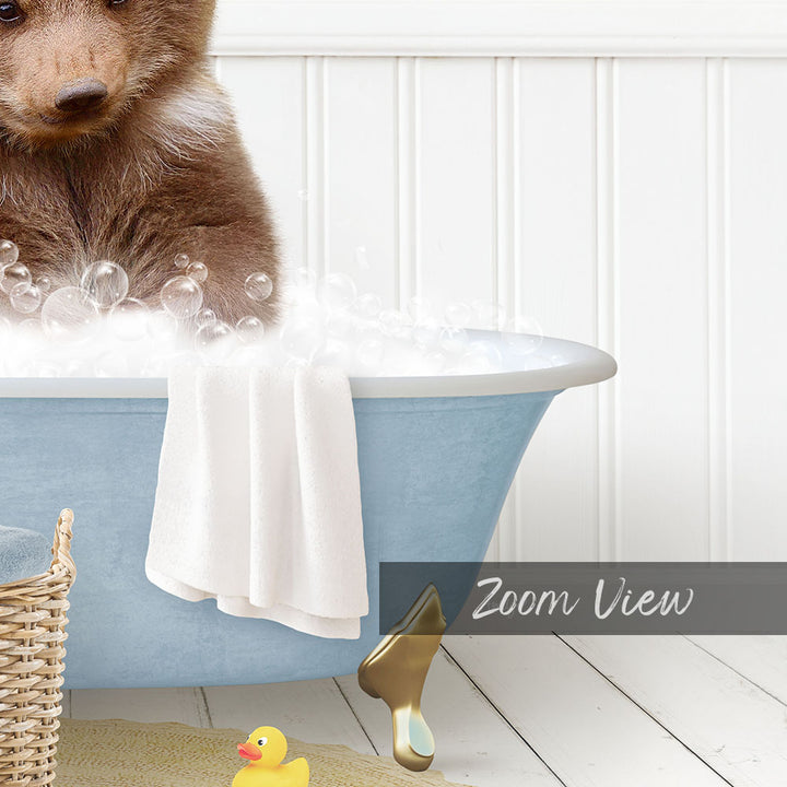 A small brown bear is sitting in a blue bathtub filled with bubbles, surrounded by a yellow rubber duck and a white towel.