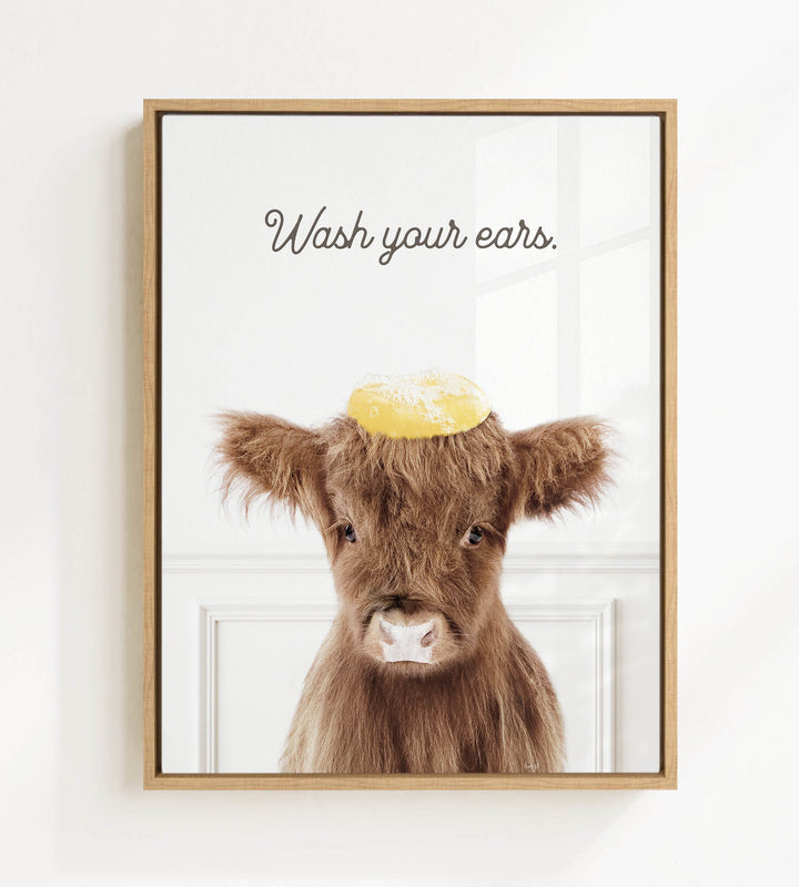 A framed image of a brown cow with a yellow object on its head, accompanied by the text "Wash your ears."