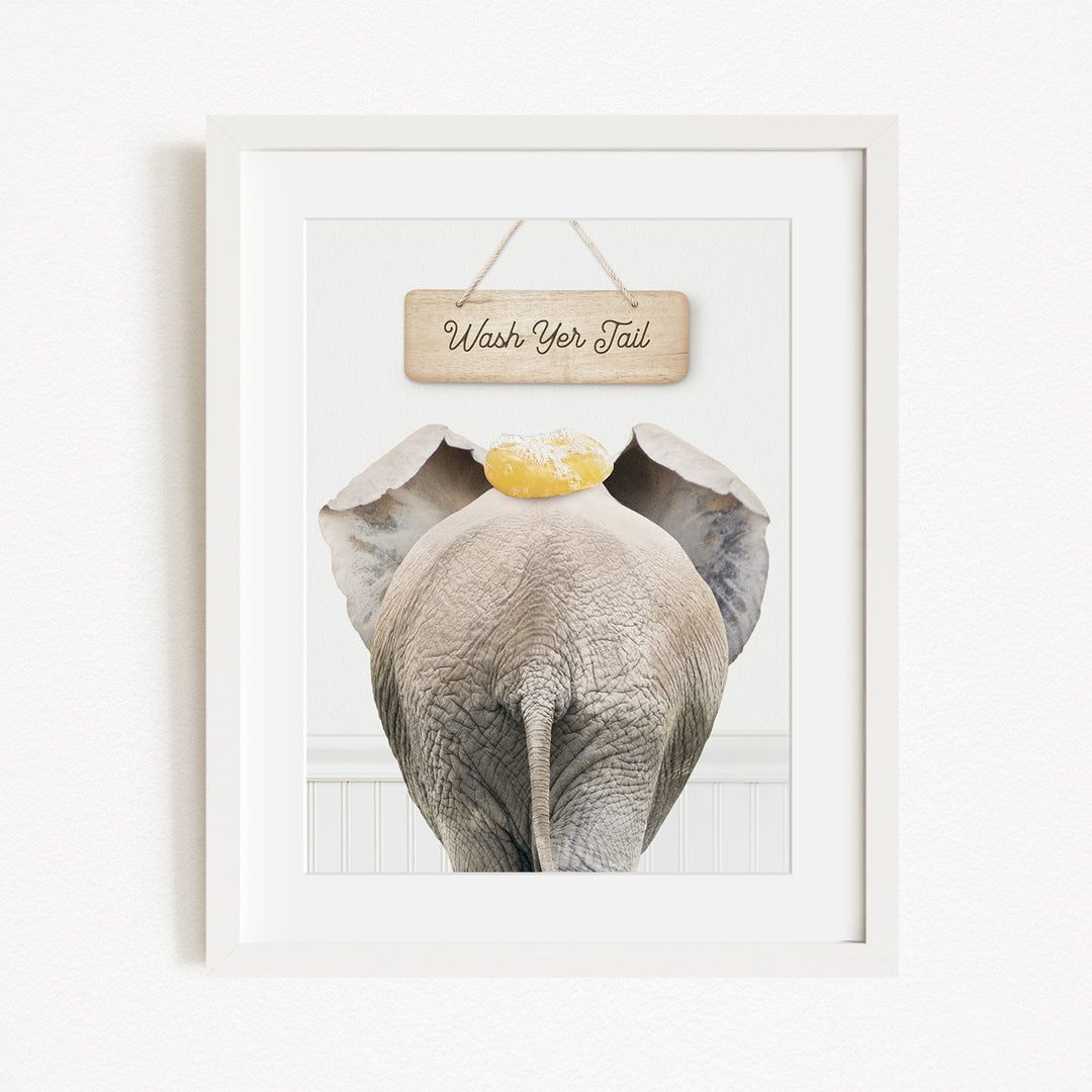A framed image of an elephant with a sign above it that says "Wash Your Tail".