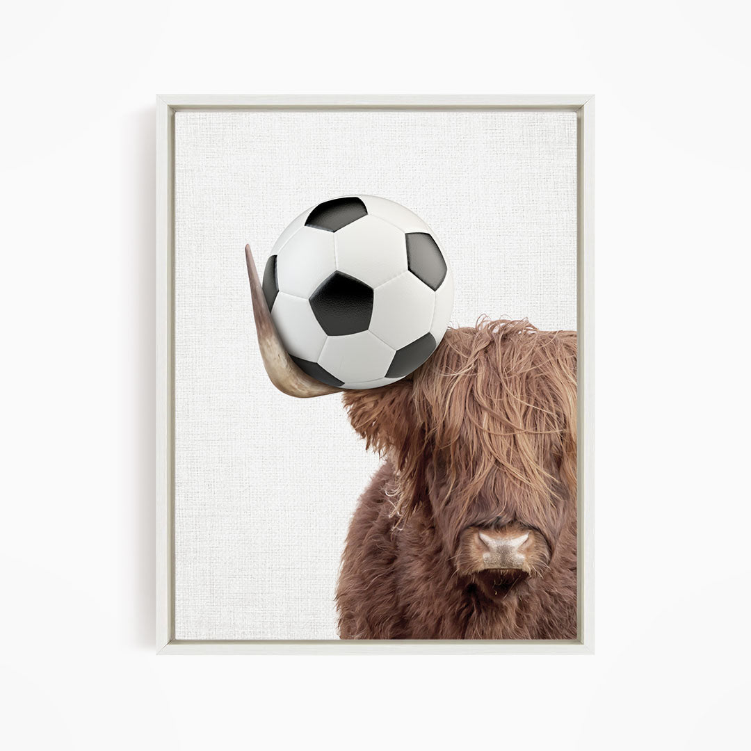 A brown cow with long hair is balancing a soccer ball on its head.