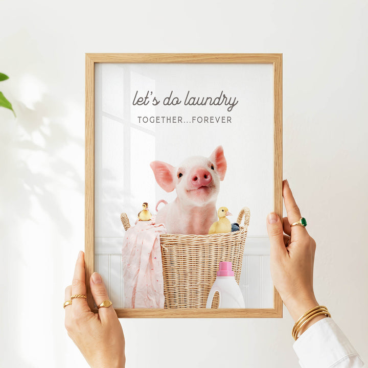 A person is holding up a framed picture of a pig sitting in a wicker basket, surrounded by various objects such as a bottle, a cup, and a toy duck.
