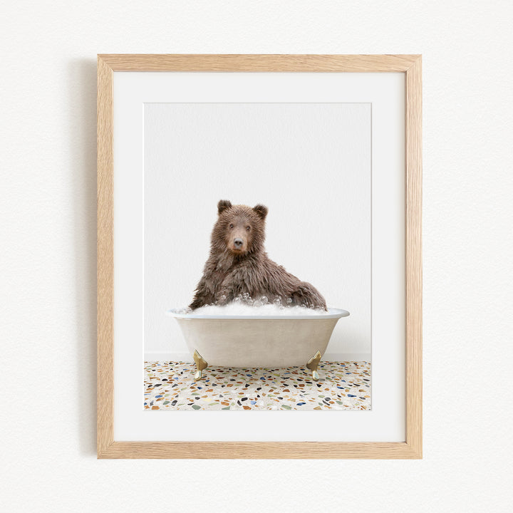 A brown bear sitting in a white bathtub filled with water, surrounded by a tiled floor.