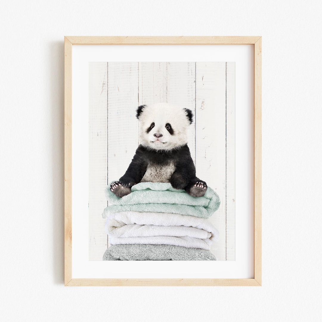 A panda bear sitting on a stack of light blue towels against a white wooden background.