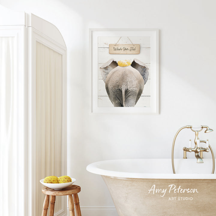 a bathroom with a framed elephant picture on the wall, a wooden stool with a bowl of fruit, and a clawfoot bathtub with a gold faucet.