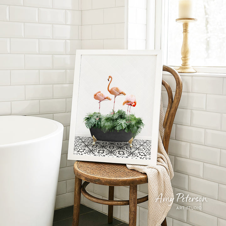 A framed image of three flamingos standing in a potted plant is displayed on a wooden chair in a bathroom setting.