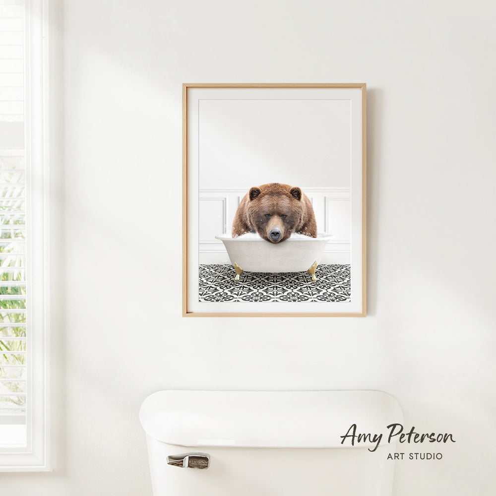 A framed image of a brown bear sitting in a bathtub is hanging on a white wall in a bathroom.