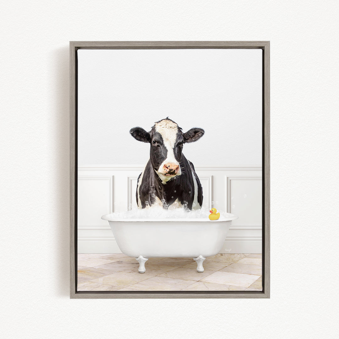 A black and white cow is standing in a white bathtub filled with water, with a rubber duck floating in the tub.