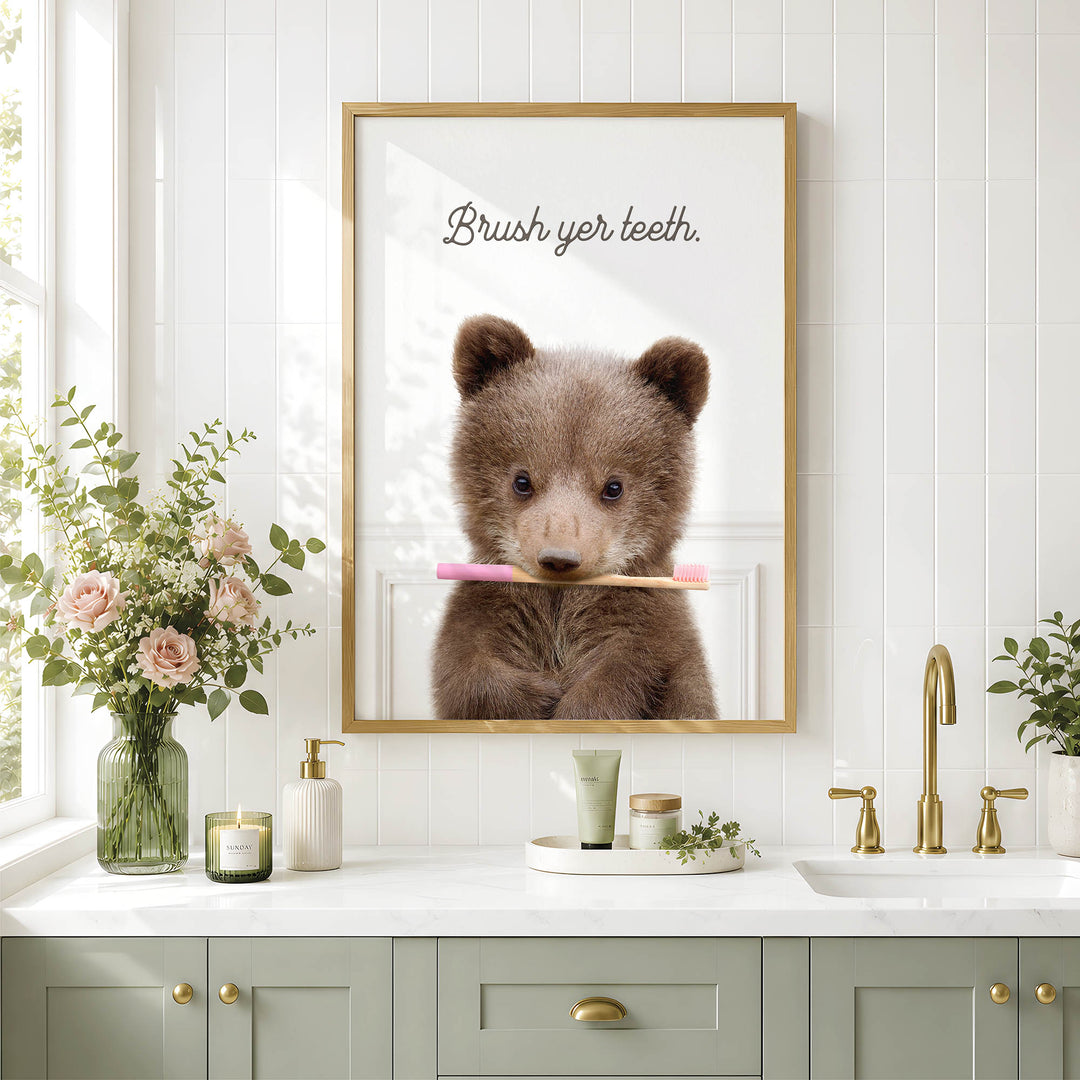 a bathroom scene with a framed photo of a bear holding a toothbrush, a vase of flowers, and a sink with a green cabinet.