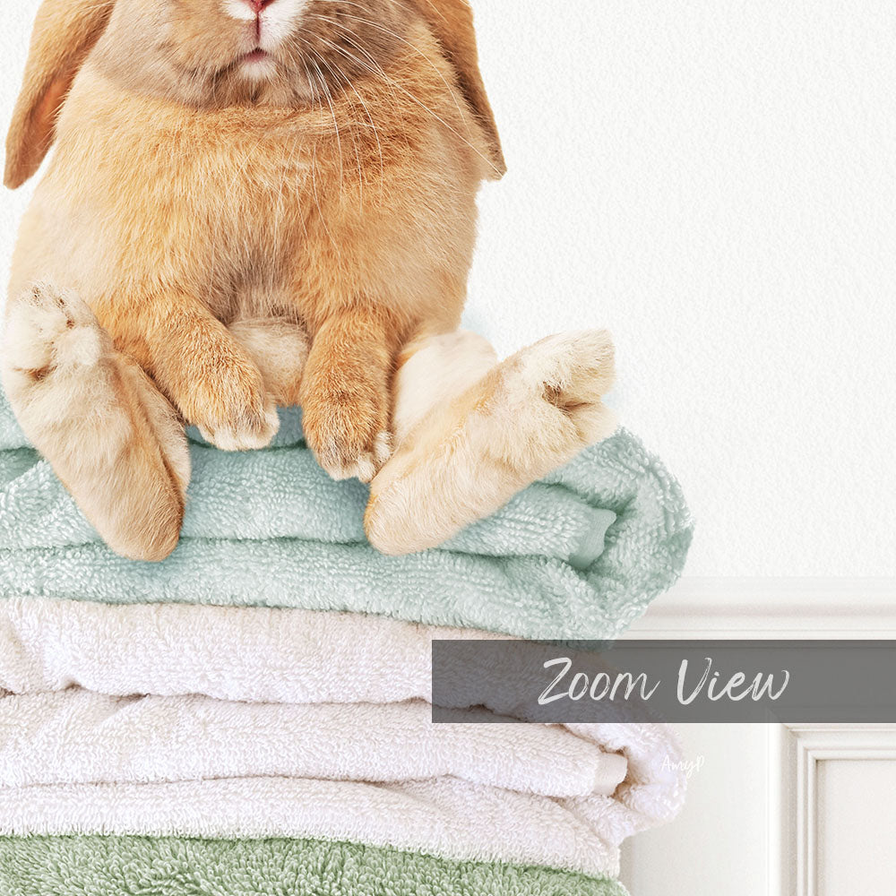 A fluffy orange rabbit sitting on a stack of light blue and white towels.