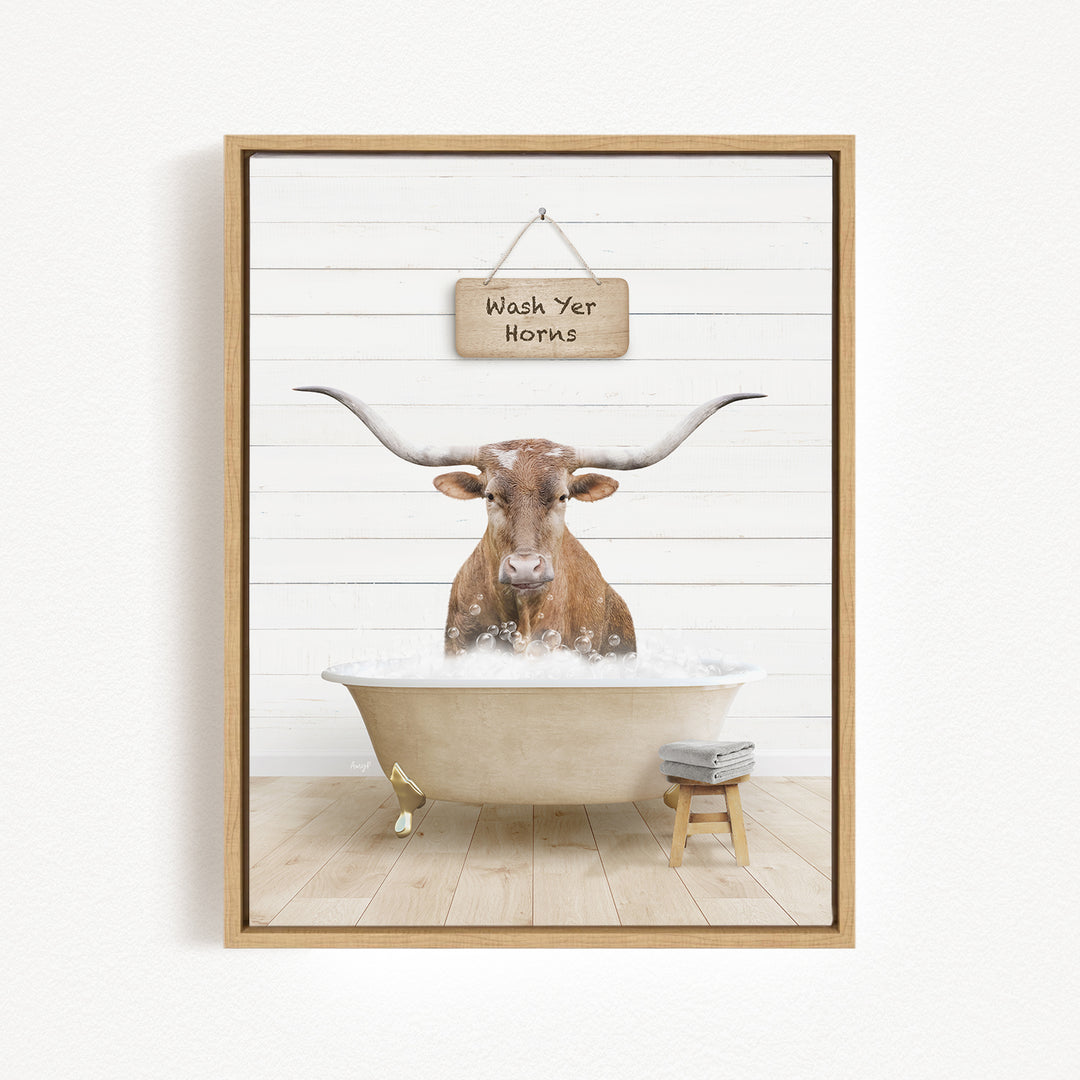 A framed image depicting a bull with large horns sitting in a bathtub, with a sign above that says "Wash Your Horns".