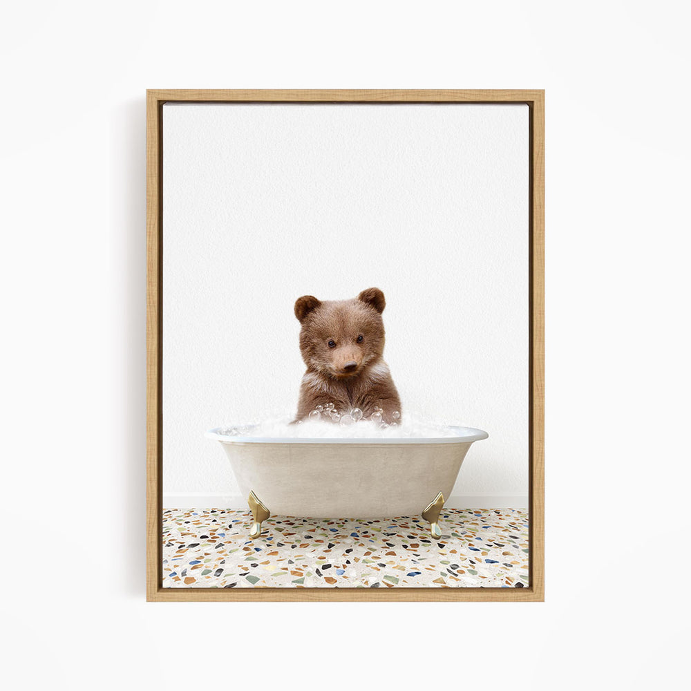 A cute brown bear cub sitting in a white bathtub filled with water, looking directly at the camera.