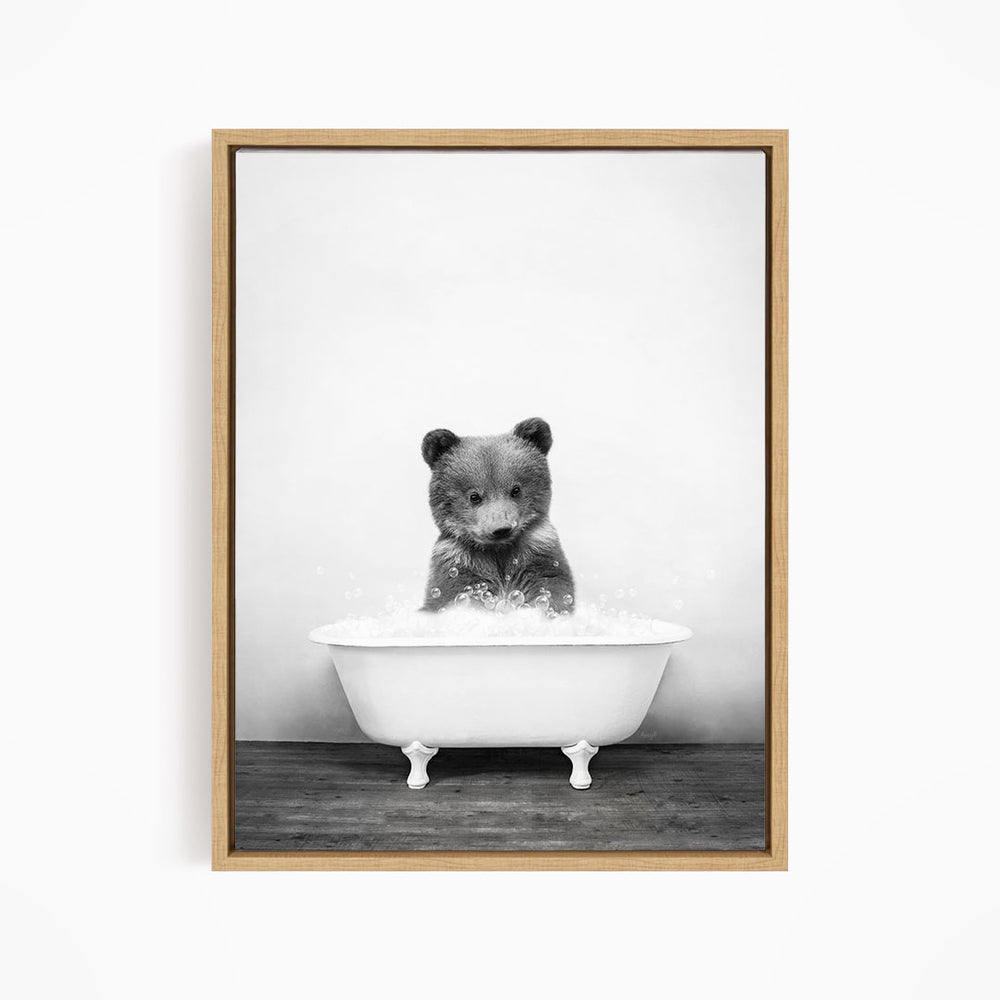 A black and white image of a bear sitting in a bathtub filled with water.
