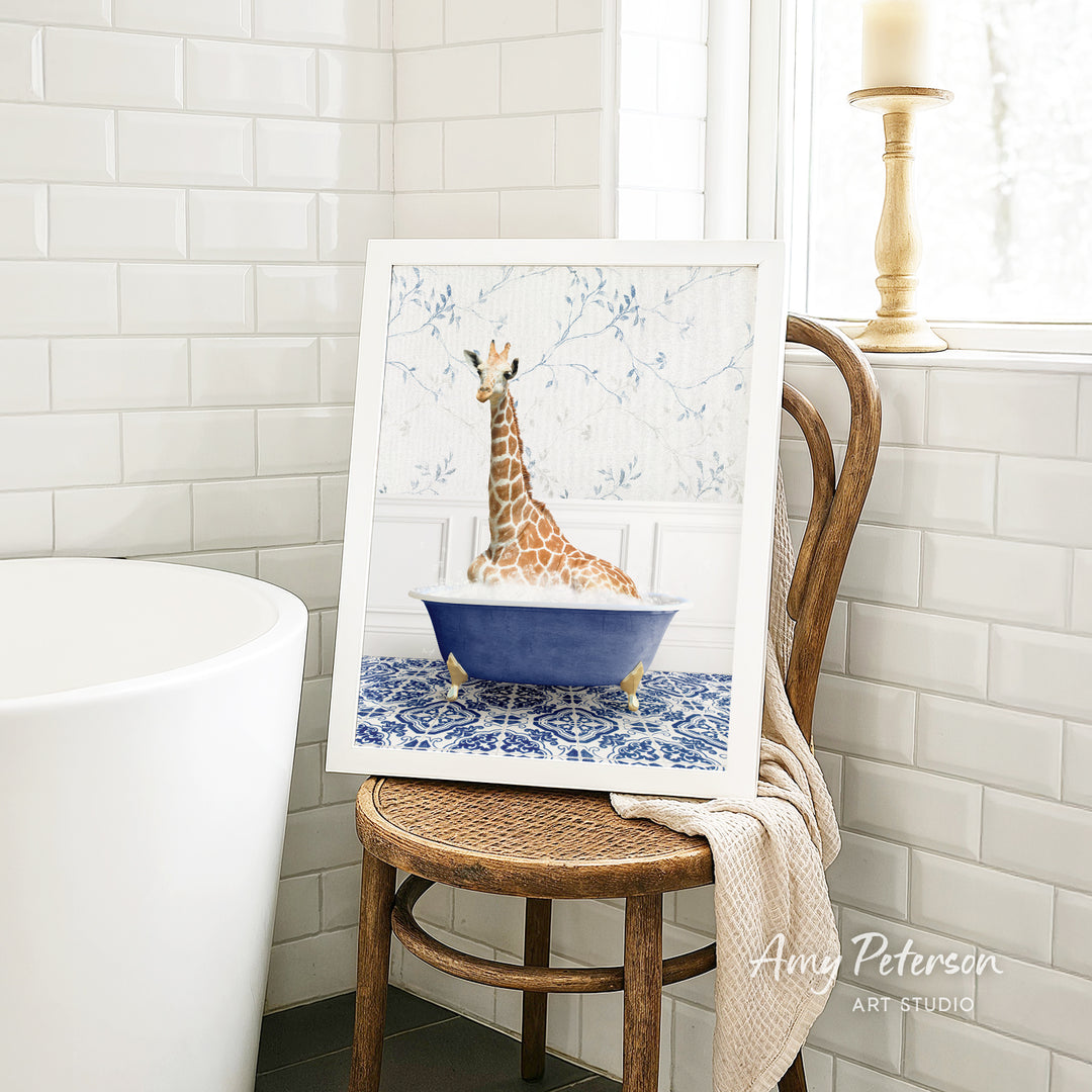 A framed painting of a giraffe sitting in a blue bathtub is displayed on a wooden chair in a bathroom setting.