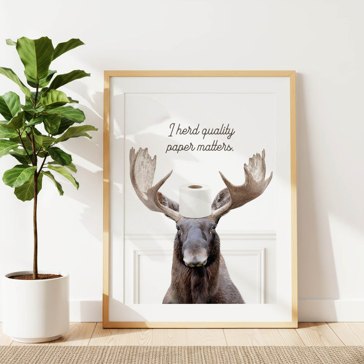 a framed print of a moose with a roll of toilet paper on its head, accompanied by the text "Thered quality paper matters."