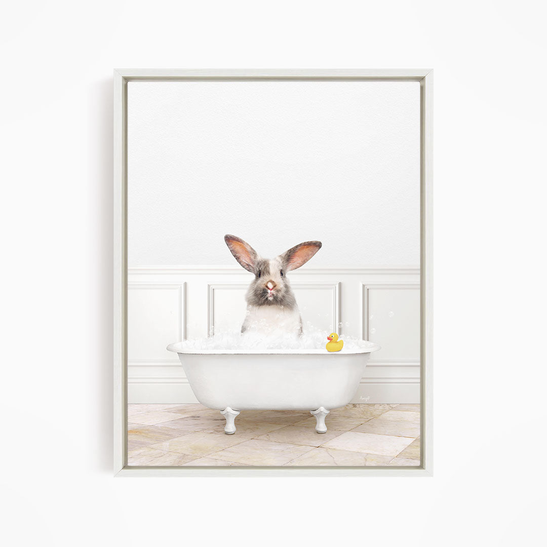 A white rabbit sitting in a white bathtub filled with water, with a rubber duck floating in the water.